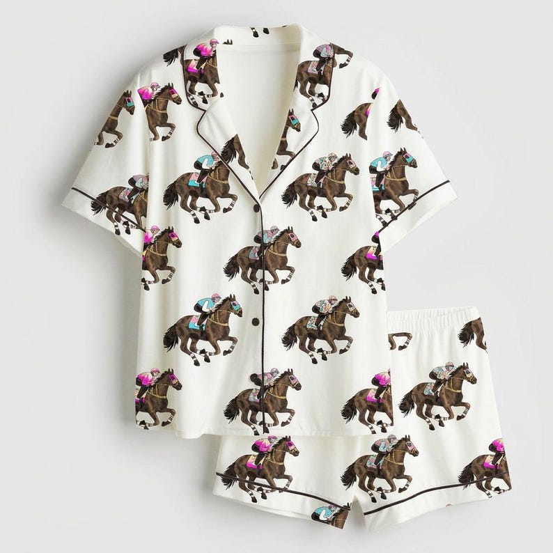 K&ouml;nnte beinhalten: Wei&szlig;es Pyjama-Set mit einem sich wiederholenden Muster aus braunen Pferden und Jockeys in verschiedenen Farben. Das kurz&auml;rmelige Oberteil und die Shorts haben schwarze Paspeln. Das Pyjama-Set ist aus einem weichen, leichten Stoff gefertigt.