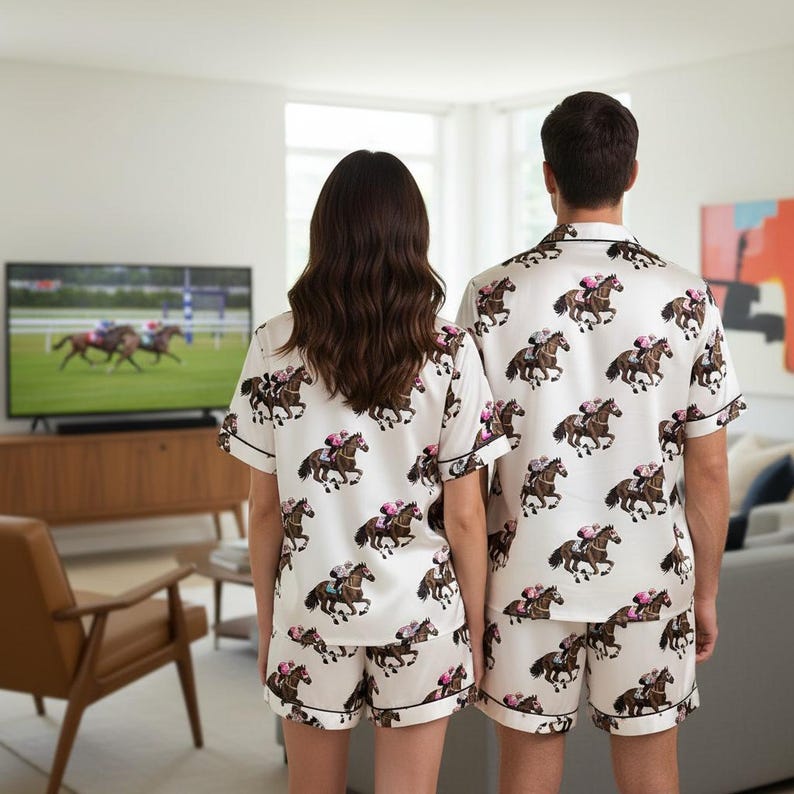K&ouml;nnte beinhalten: Passende wei&szlig;e Pyjama-Sets mit einem Pferderenn-Print. Jedes Set besteht aus einem kurz&auml;rmeligen Hemd mit Kn&ouml;pfen und Shorts. Die Pyjamas haben schwarze Paspeln und zeigen braune Pferde mit rosafarbenen Jockeys.