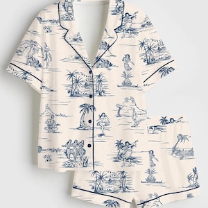 May include: Cream-colored pajama set featuring a navy blue tropical print. The set includes a short-sleeved button-down shirt and matching shorts. The print depicts island scenes with palm trees, dancers, and musicians.