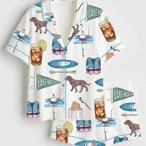 Peut inclure: Ensemble de pyjama blanc avec un motif r&eacute;p&eacute;t&eacute; de chiens bruns, de flotteurs de p&ecirc;che, de gilets de sauvetage, de kayaks et de cocktails. L'ensemble chemise et short a une bordure bleue et les mots "LAKE HOUSE" sur un fanion.