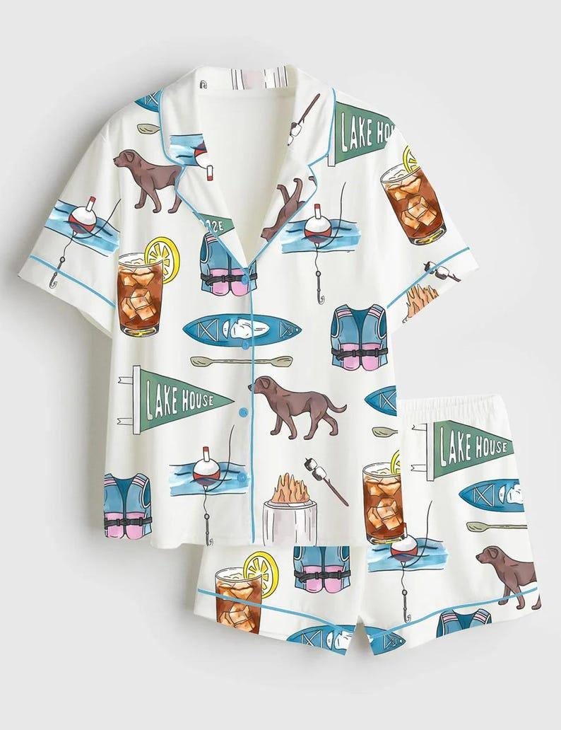 Peut inclure: Ensemble de pyjama blanc avec un motif r&eacute;p&eacute;t&eacute; de chiens bruns, de flotteurs de p&ecirc;che, de gilets de sauvetage, de kayaks et de cocktails. L'ensemble chemise et short a une bordure bleue et les mots "LAKE HOUSE" sur un fanion.