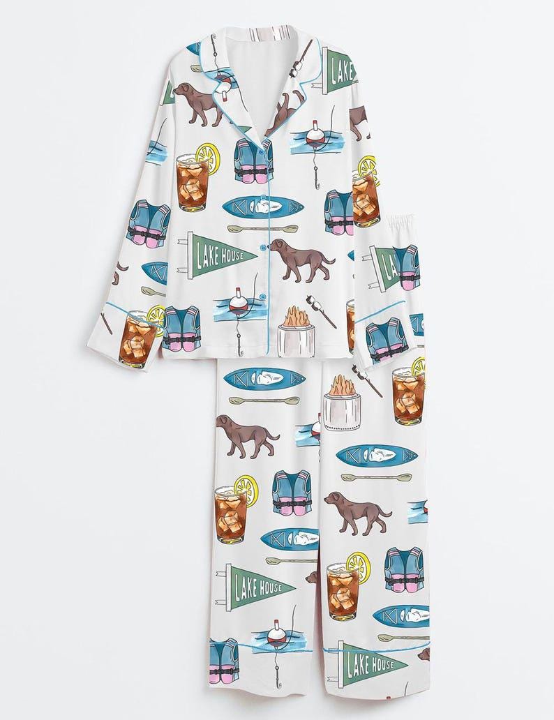 Peut inclure: Ensemble de pyjama blanc avec un motif r&eacute;p&eacute;t&eacute; d'illustrations sur le th&egrave;me du lac. Le motif comprend des chiens bruns, des gilets de sauvetage, des kayaks, des flotteurs de p&ecirc;che, des cocktails au citron et des fanions avec l'inscription "LAKE HOUSE".