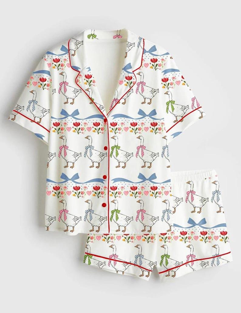 Może przedstawiać: Biały zestaw piżamowy z fantazyjnym nadrukiem gęsi. Kr&oacute;tki rękaw topu i szorty mają powtarzający się wz&oacute;r gęsi w kokardkach, czerwonych wykończeniach i kwiatowych akcentach. Zestaw zawiera koszulę zapinaną na guziki i szorty.