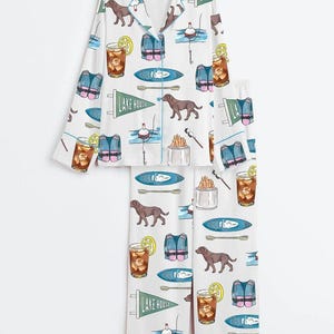 Peut inclure: Ensemble de pyjama blanc avec un motif r&eacute;p&eacute;t&eacute; d'illustrations sur le th&egrave;me du lac. Le motif comprend des chiens bruns, des gilets de sauvetage, des kayaks, des flotteurs de p&ecirc;che et des cocktails au citron. L'ensemble comprend une chemise boutonn&eacute;e &agrave; col et un pantalon assorti.