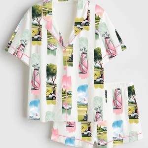 Peut inclure: Ensemble de pyjama blanc sur le th&egrave;me du golf. Le haut &agrave; manches courtes et le short pr&eacute;sentent un motif r&eacute;p&eacute;t&eacute; de sacs de golf, de voiturettes et de sc&egrave;nes de parcours en rose, vert et bleu. Bordure rose.