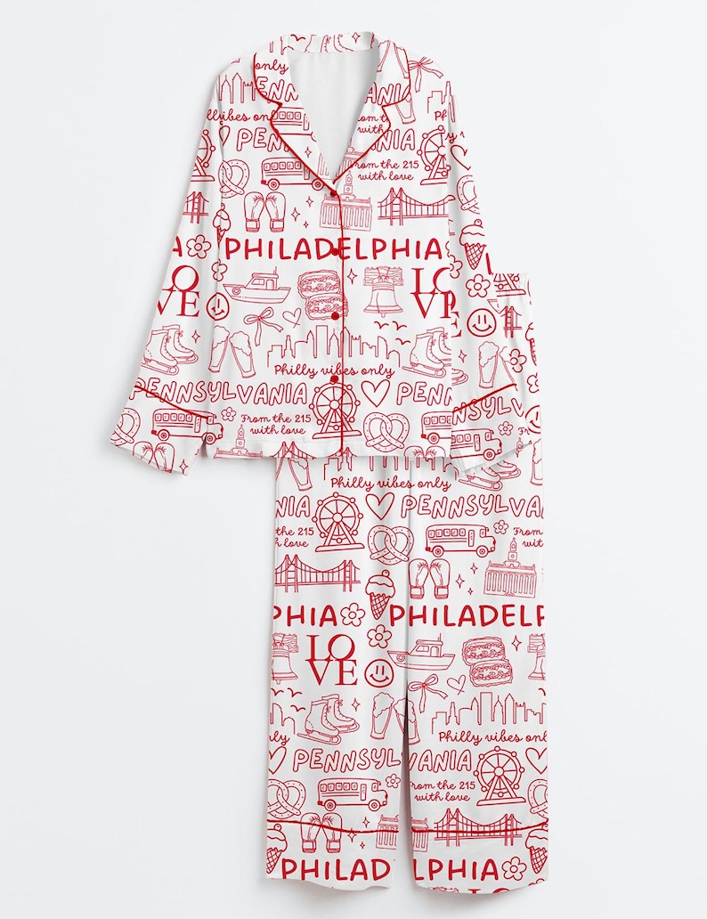 May include: White pajama set with a red Philadelphia-themed print. The set includes a button-down top and pants, featuring city landmarks, icons, and text like "Philadelphia" and "Pennsylvania". The pajamas have red trim.