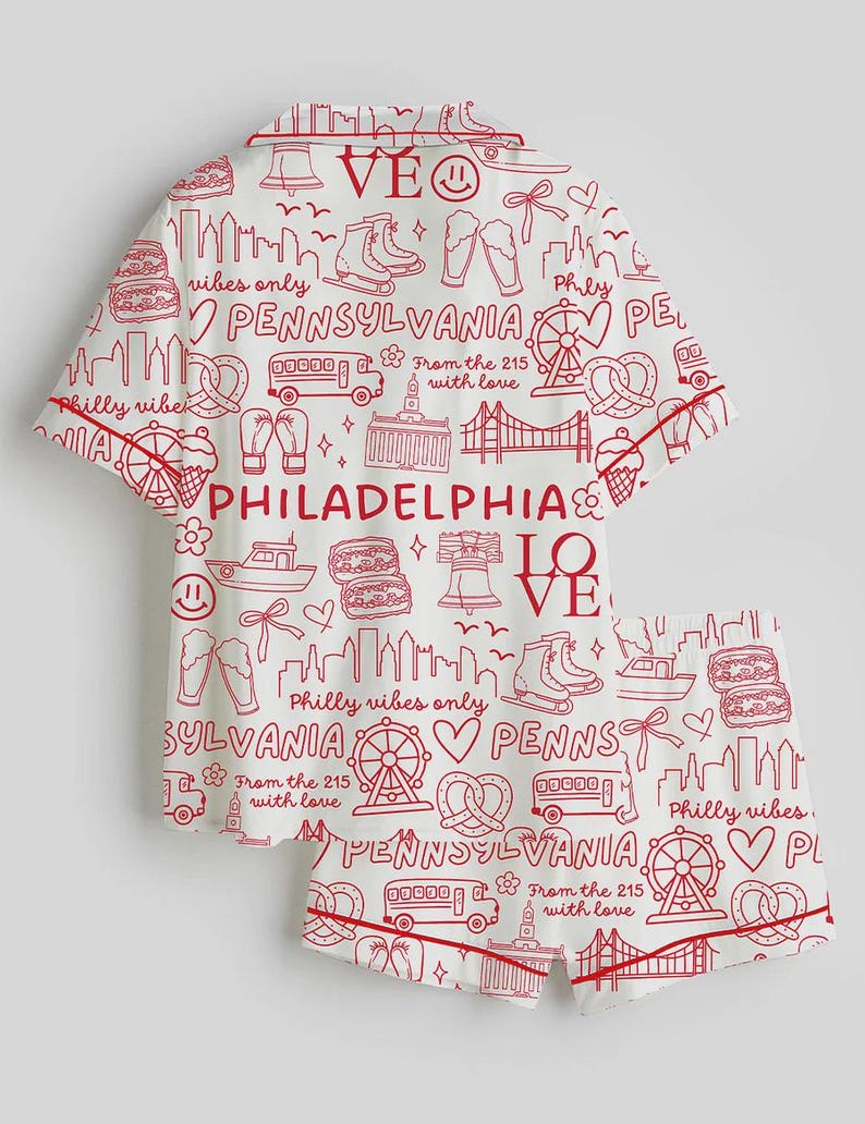May include: White pajama set with a red Philadelphia-themed print. The set includes a short-sleeved top and shorts, both featuring city landmarks, icons, and text. The trim is red.