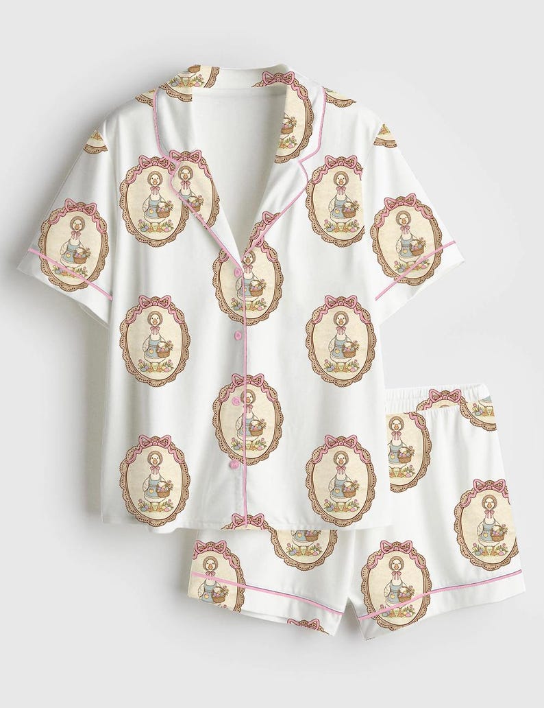 Może przedstawiać: Biały zestaw piżamowy z powtarzającym się wzorem gęsi niosącej kosz, oprawionej w owal z r&oacute;żową kokardą. Zestaw zawiera koszulę zapinaną na guziki z kr&oacute;tkim rękawem i pasujące szorty, wykończone r&oacute;żową lam&oacute;wką.