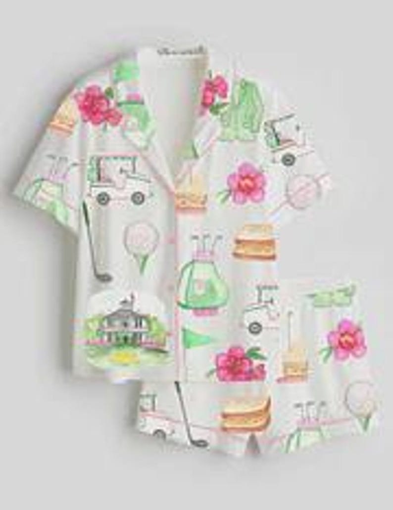 May include: White pajama set with a golf-themed pattern. The set includes a short-sleeved button-down shirt and matching shorts. The pattern features golf carts, golf balls, pink flowers, and a golf course scene.