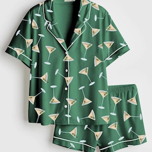 K&ouml;nnte beinhalten: Gr&uuml;nes Pyjama-Set mit Martini-Muster. Das kurz&auml;rmelige Oberteil und die Shorts sind mit wei&szlig;en Zierleisten und einem sich wiederholenden Design von Martinigl&auml;sern mit Oliven versehen. Das Set ist aus einem weichen, leichten Stoff gefertigt.