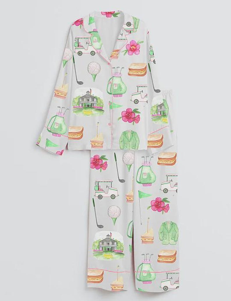 May include: Light gray pajama set with a golf-themed pattern. The set features a button-down top and pants, adorned with golf carts, golf balls, golf clubs, sandwiches, pink flowers, and a green golf course. The trim is pink.