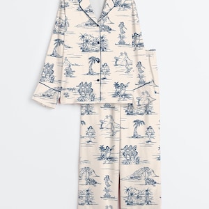 May include: A two-piece pajama set in a cream color with a blue island-themed print. The long-sleeved top has a button-down front and navy trim. The matching pants have a relaxed fit. The print features palm trees, dancers, and musicians.