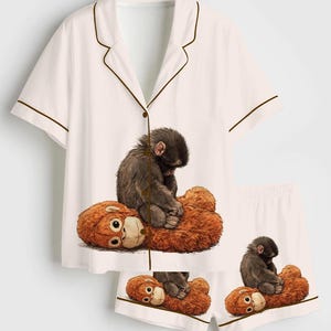May include: White pajama set with a brown trim, featuring a graphic of a monkey sitting on a teddy bear. The set includes a short-sleeved top and matching shorts, perfect for a cozy night's sleep.