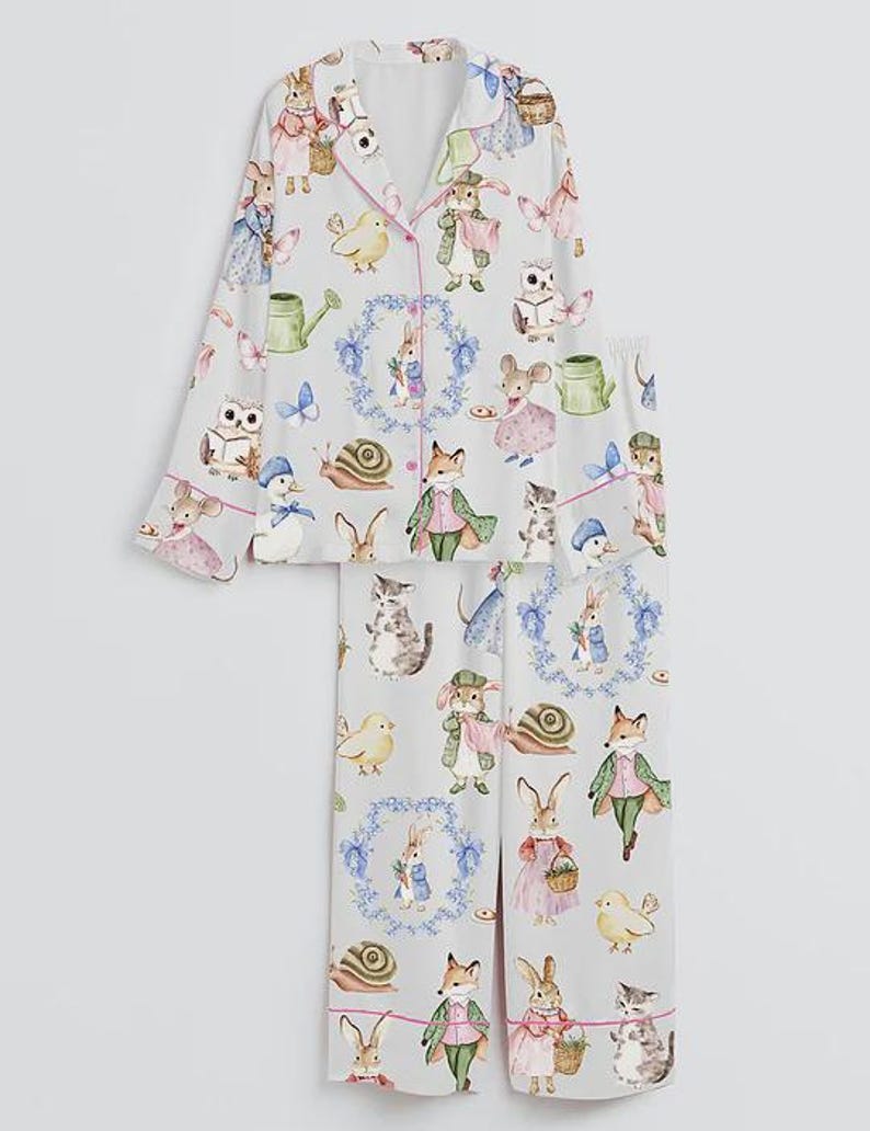 May include: Light gray pajama set with a whimsical print of woodland creatures, including rabbits, foxes, and owls. The long-sleeved top and pants feature pink piping and a button-down front. The pajama set is made of a soft, lightweight fabric.