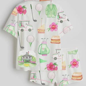 May include: White pajama set with a golf-themed watercolor print. The set includes a short-sleeved button-up shirt and shorts. The print features golf balls, golf carts, sandwiches, pink flowers, golf clubs, and a green blazer.
