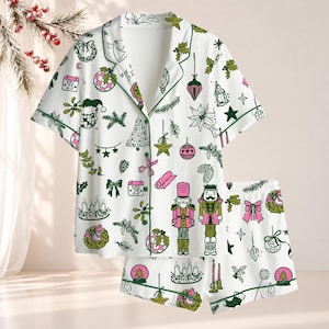 May include: A white short-sleeve pajama set featuring a repeating pattern of Christmas-themed illustrations in pink, green, and black. The print includes nutcrackers, calendars marked Dec 25, ornaments, bows, candles, and pine branches.