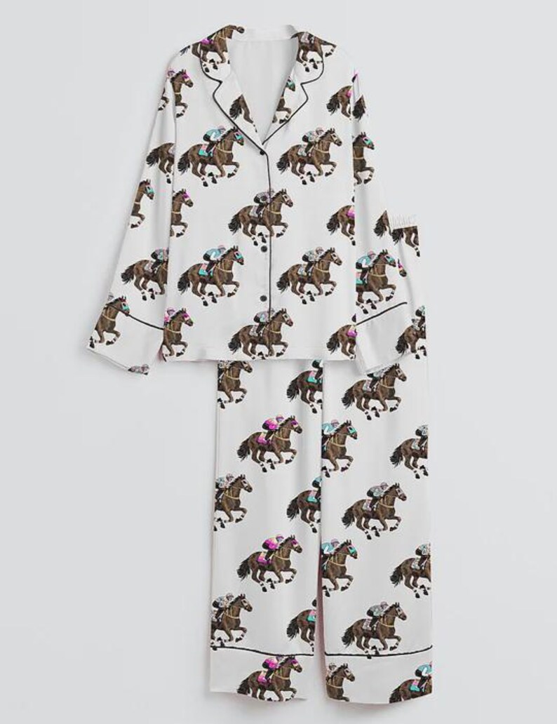 K&ouml;nnte beinhalten: Wei&szlig;es Pyjama-Set mit einem sich wiederholenden Muster aus braunen Rennpferden und Jockeys. Das lang&auml;rmlige Oberteil hat schwarze Paspeln und Kn&ouml;pfe. Die passende Hose hat ebenfalls schwarze Paspeln.