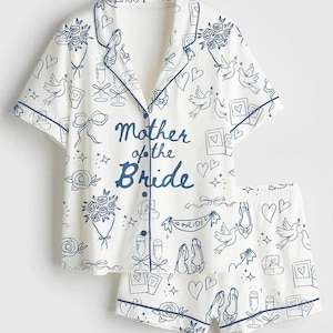 May include: A white pajama set with a short-sleeved shirt and shorts. The set is patterned with blue outlines of doves, hearts, flowers, and the text "Mother of the Bride". The edges of the set are trimmed with blue piping.