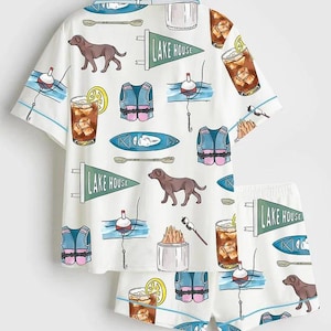 Peut inclure: Ensemble de pyjama blanc avec un motif r&eacute;p&eacute;t&eacute; de chiens bruns, de gilets de sauvetage, de flotteurs de p&ecirc;che, de kayaks et de cocktails. L'ensemble chemise et short comporte &eacute;galement le texte "LAKE HOUSE" sur des fanions.