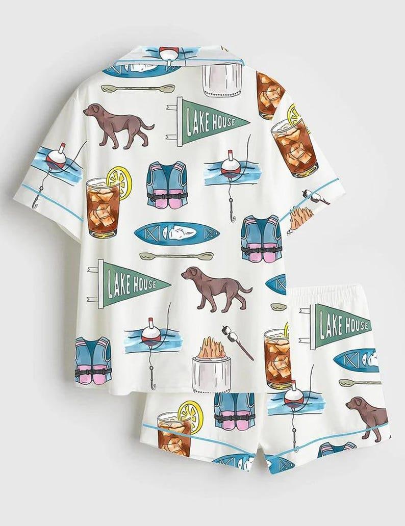 Peut inclure: Ensemble de pyjama blanc avec un motif r&eacute;p&eacute;t&eacute; de chiens bruns, de gilets de sauvetage, de flotteurs de p&ecirc;che, de kayaks et de cocktails. L'ensemble chemise et short comporte &eacute;galement le texte "LAKE HOUSE" sur des fanions.