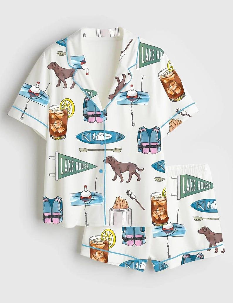 Peut inclure: Ensemble de pyjama blanc avec un motif r&eacute;p&eacute;t&eacute; de chiens bruns, de flotteurs de p&ecirc;che, de gilets de sauvetage, de kayaks et de cocktails. L'ensemble chemise et short a une bordure bleue et les mots "LAKE HOUSE" sur un fanion.