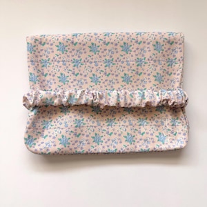 May include: A rectangular fabric pouch featuring a light pink background with a repeating floral pattern in shades of blue and green. The pouch has a horizontal gathered elastic band across the center and a small white embroidered goose outline.