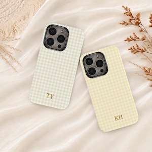 May include: Two smartphone cases featuring a gingham pattern in light green and light yellow. Each case has a black camera cutout and gold-colored initials printed on the lower section, with one case displaying the letters TY and the other KH.
