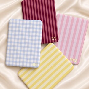 Puede incluir: Cuatro estuches rectangulares con esquinas redondeadas que presentan patrones distintos: un vichy azul claro, una raya vertical roja oscura, una raya vertical rosa claro y una raya vertical amarilla. Cada estuche muestra iniciales doradas: BP, RT, MKZ.