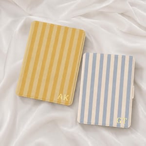 May include: Two rectangular cases with vertical stripes. The larger case features yellow and cream stripes with the gold-colored initials AK in the bottom right corner. The smaller case features blue and cream stripes with the gold-colored initials GT.