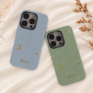 Op de afbeelding: Twee smartphonehoesjes in lichtblauw en saliegroen, elk voorzien van een goudkleurig foliepatroon van maansikkels en sterren. Het blauwe hoesje is gepersonaliseerd met de naam Katie en het groene hoesje met de naam Rose.