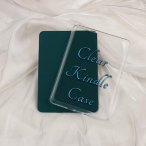 Könnte beinhalten: Eine tealfarbene Kindle-Hülle mit einer transparenten Schutzhülle. Auf der transparenten Hülle steht in hellblauer Schrift "Clear Kindle Case". Die Hülle liegt auf einem weißen, seidigen Hintergrund.