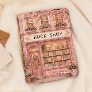 Puede incluir: Una lata rectangular de metal con una ilustración impresa de una librería rosa con escaparate, grandes ventanales con filas de libros, una puerta principal con una corona y flores en macetas. El texto BOOK SHOP aparece sobre las ventanas.