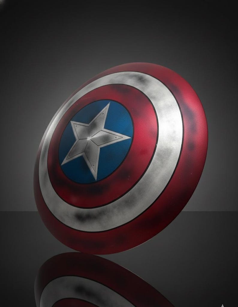 May include: A round shield with a red, white, and blue color scheme. The shield features a white star on a blue center, surrounded by concentric red and white bands. The shield is slightly angled, with a reflection visible below.