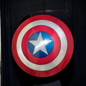 May include: A red, white, and blue shield with a silver star in the center. The shield has a circular design with concentric rings of red, white, and silver. The center is blue with a white star.
