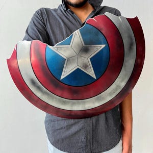 May include: A Captain America shield with a distressed finish. The shield features a central white star on a blue circle, surrounded by red and white stripes. The shield has a battle-worn appearance.