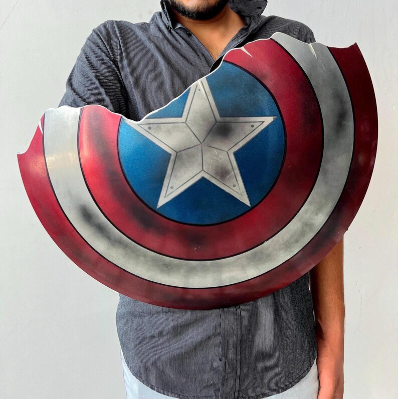 May include: A Captain America shield with a distressed finish. The shield features a central white star on a blue circle, surrounded by red and white stripes. The shield has a battle-worn appearance.