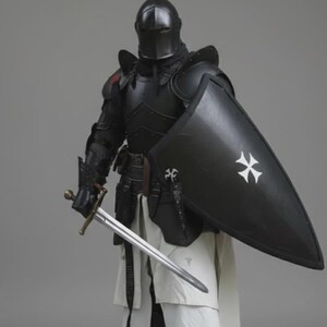 Puede incluir: Una armadura negra completa, que incluye un casco, protectores de hombros y peto. El caballero sostiene una espada larga y un escudo negro con una cruz blanca. El caballero lleva una t&uacute;nica blanca y botas negras.