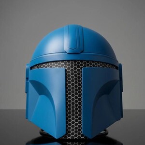 Puede incluir: Un casco azul con una malla de panal negra que cubre el &aacute;rea de la cara. El casco tiene un acabado liso y mate y est&aacute; dise&ntilde;ado con elementos angulares. El casco es probablemente un accesorio o un objeto de colecci&oacute;n.