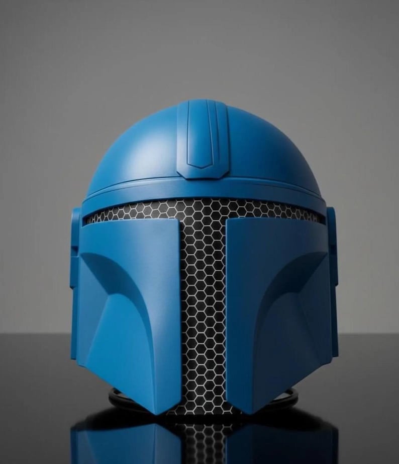Puede incluir: Un casco azul con una malla de panal negra que cubre el &aacute;rea de la cara. El casco tiene un acabado liso y mate y est&aacute; dise&ntilde;ado con elementos angulares. El casco es probablemente un accesorio o un objeto de colecci&oacute;n.