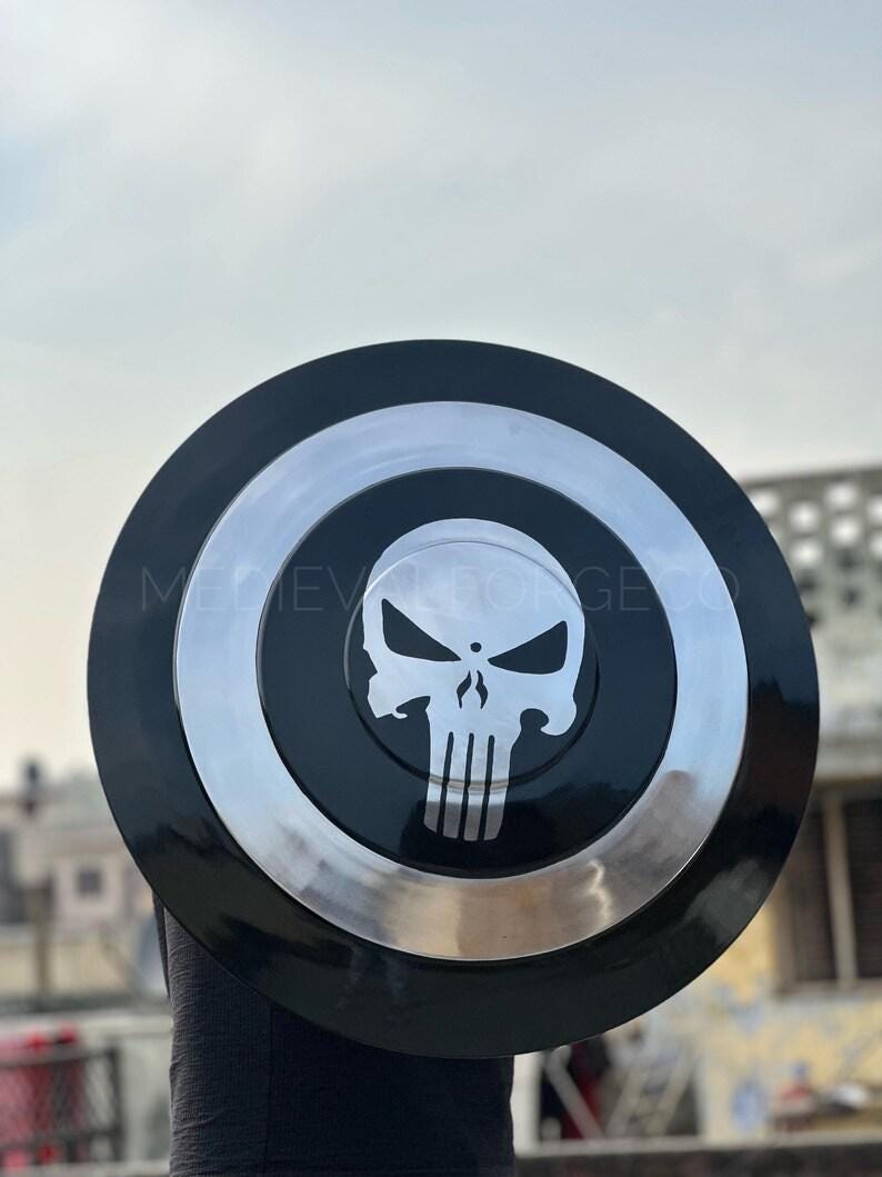 May include: A black and silver shield featuring a white skull emblem. The shield has a circular design with a black outer ring, a silver inner ring, and a black center with the skull logo. The text "MEDIEVAL FORGE CO" is visible.