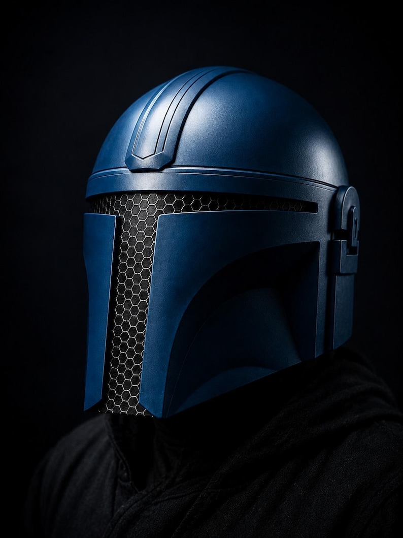 Puede incluir: Un casco azul mandaloriano con una visera de malla de panal. El casco tiene un dise&ntilde;o elegante y angular sobre un fondo oscuro. Es un art&iacute;culo de cosplay.