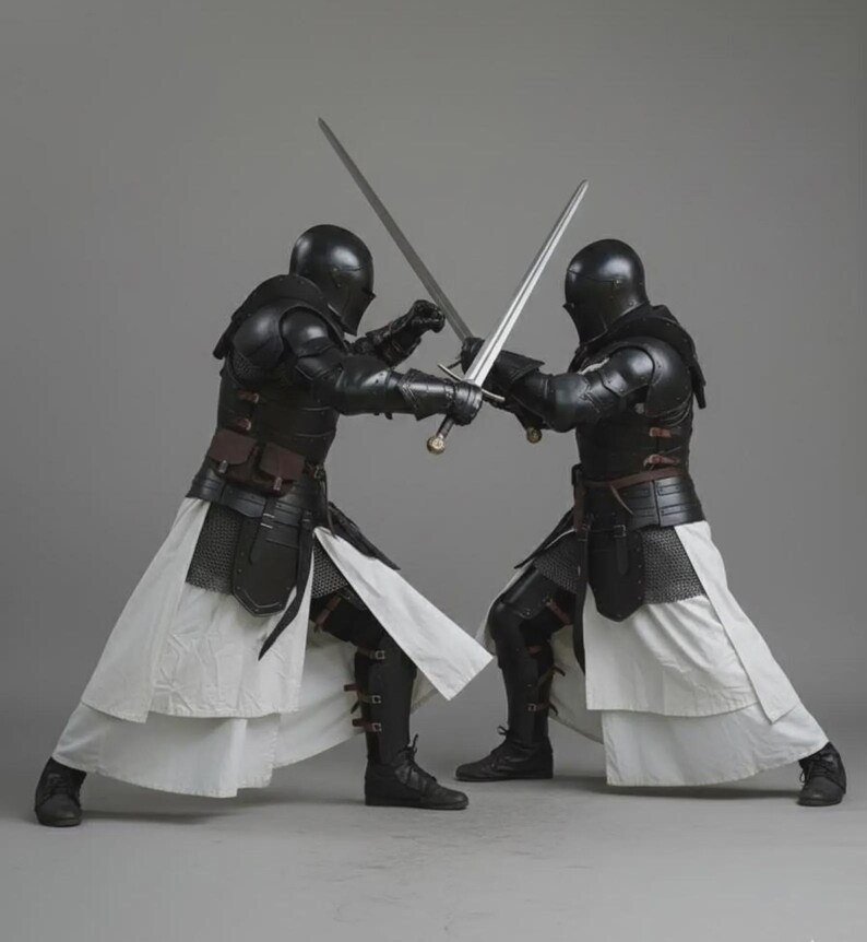 Puede incluir: Dos figuras con armadura negra, cascos y faldas blancas se enfrentan en un combate con espadas. Las figuras sostienen espadas con hojas plateadas y empu&ntilde;aduras doradas. La armadura incluye protecci&oacute;n para hombros y pecho, con detalles de cuero y cota de malla.