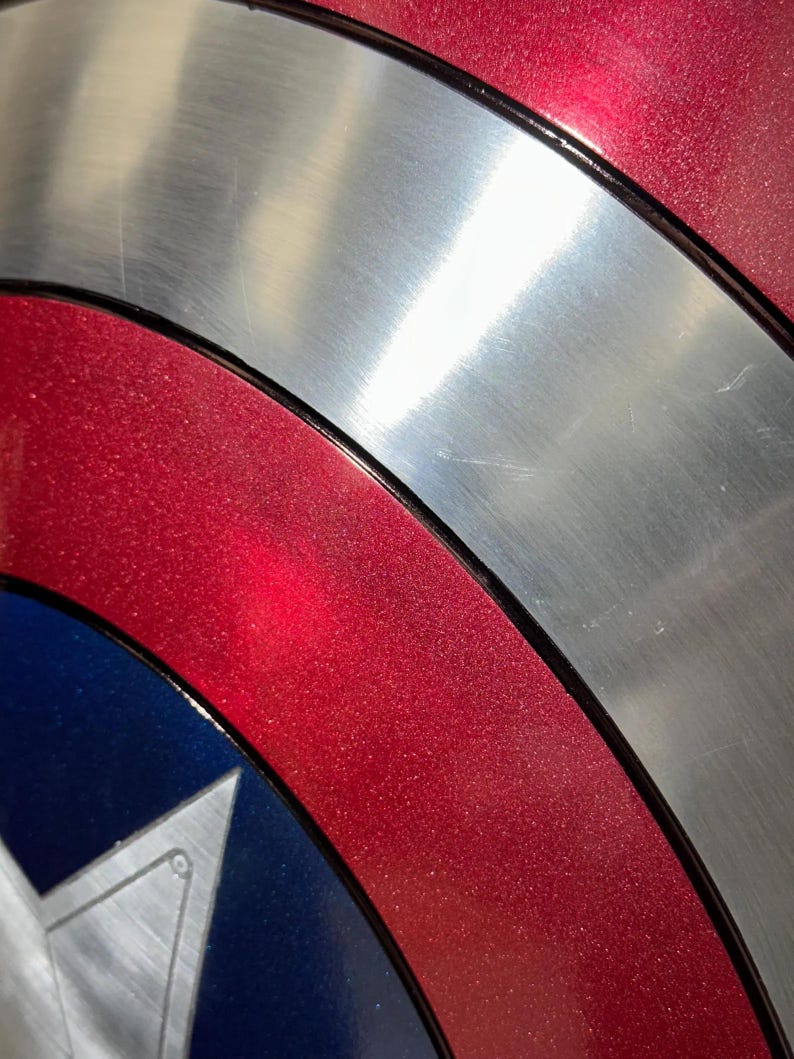May include: Close-up of a Captain America shield. The shield features a metallic silver center, bordered by a red ring with a glittery texture. A blue section with a white star is visible.