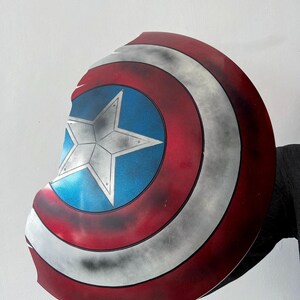 May include: A Captain America shield prop, featuring a red, white, and blue color scheme. The shield has a central blue circle with a white star, surrounded by red and white stripes. The shield is slightly weathered.