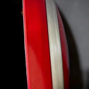 May include: A red and silver shield with a glossy finish. The shield has a bright red section and a silver stripe. The edges are smooth and the overall shape is rounded.
