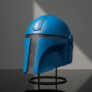 Puede incluir: Casco azul con visera de malla negra, exhibido sobre un soporte de metal negro. El casco tiene un acabado liso y mate y un dise&ntilde;o que recuerda a un guerrero futurista. El soporte es circular, proporcionando una base estable.