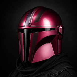 Może przedstawiać: Metalowy czerwony hełm z czarnymi detalami, z wizjerem i kanciastym designem. Hełm jest częścią kostiumu, prawdopodobnie do cosplayu lub ekspozycji, i jest umieszczony na ciemnym tle.