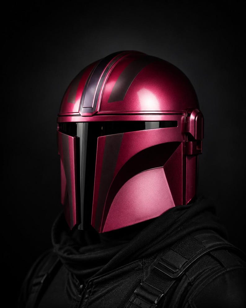 Może przedstawiać: Metalowy czerwony hełm z czarnymi detalami, z wizjerem i kanciastym designem. Hełm jest częścią kostiumu, prawdopodobnie do cosplayu lub ekspozycji, i jest umieszczony na ciemnym tle.