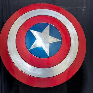May include: A round shield with a red outer ring, a silver inner ring, and a blue center. A silver five-pointed star is in the center. The shield is a replica of Captain America's shield.