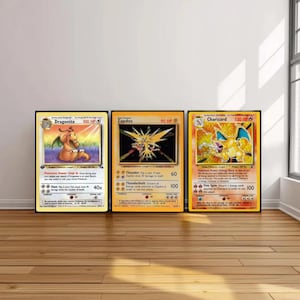 Könnte beinhalten: Drei gerahmte Pokémon-Sammelkarten mit Dragonite, Zapdos und Glurak. Die Karten werden auf einem Holzboden mit einer weißen Wand und einem Fenster im Hintergrund ausgestellt. Die Glurak-Karte hat 120 KP.